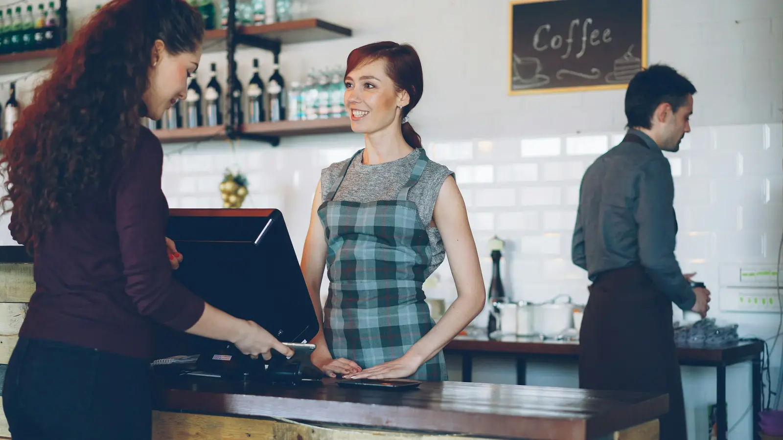 Cafe owner behind the till, smiling at a customer who is paying